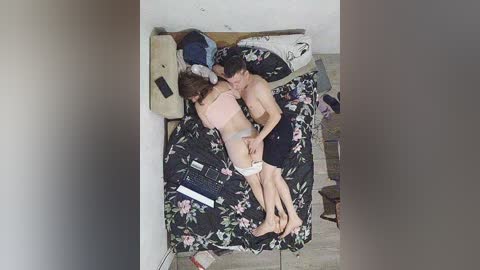 Video of a topless man and a nude woman embracing on a bed with floral sheets in a cluttered, dimly lit room.