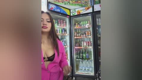 Video of a curvy woman with long brown hair, wearing a pink shirt and black bra, in a brightly lit convenience store with colorful drink displays and shelves.