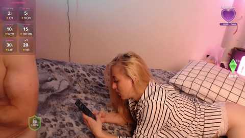 Video of a blonde woman in a striped top lying on a bed, watching TV, with a virtual overlay showing health stats.