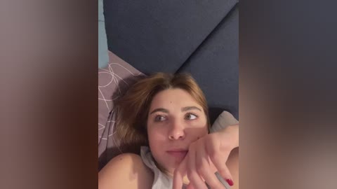 Video of a light-skinned woman with light brown hair, lying on a blue couch with a grey pillow, resting her head on her hand, looking thoughtful.