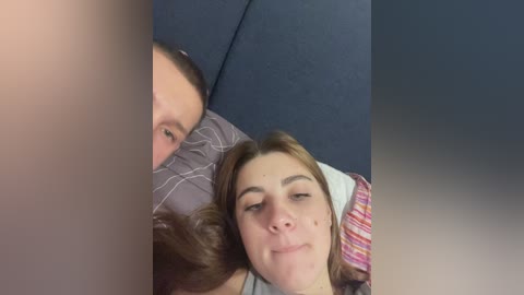 Video of a close-up, blurred selfie showing a woman with brown hair and freckles sleeping next to a man with short hair, both on a blue couch.