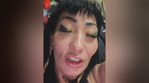 Video of a close-up of an Asian woman with short black hair, wearing heavy green and gold eyeshadow, red lipstick, and large gold hoop earrings. She appears to be singing or speaking passionately.
