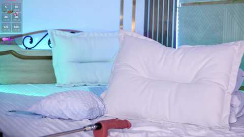 Video of a neatly made bed with white pillows and a rolled-up white blanket on a light wooden headboard, a red hairbrush on the bedspread, and a metal bed frame in the background.