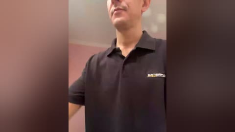 Video of a man in a black polo shirt with a white logo and name tag, standing indoors with blurred background.