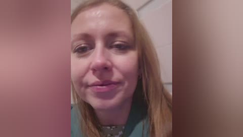 Video of a smiling Caucasian woman with fair skin and light brown hair, wearing a green top, taken from a close-up angle, with blurred background.