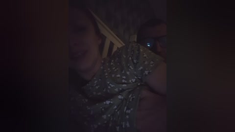 Video of a woman with medium skin tone and dark hair, wearing a floral-patterned dress, partially obscured by darkness. Her face is partially visible, showing a relaxed expression.