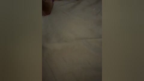 A dimly lit video showing a person's hand touching a bedsheet with a light beige color, creating a sense of intimacy and vulnerability.