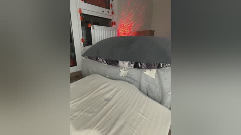 Video of a messy bedroom with a ripped duvet cover revealing a gray blanket beneath, a white radiator, and a red string light casting a glow on the wall.