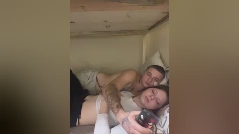 Video of a tattooed man and a sleeping woman in a small, dimly lit room with a bed and a wooden ceiling.