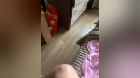 Video of a young child lying on a bed with a pink blanket, wooden floor, and a red \"Express\" bag nearby.