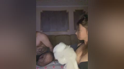 A video shows a sleeping baby on a sofa, with a white dog licking its face. The background has dimly lit walls with framed art. The scene appears intimate and tender.