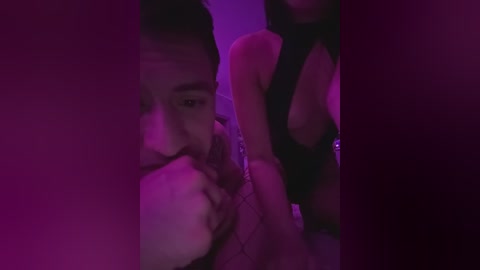 Video of a dimly lit bedroom with a man and woman, both partially clothed. The woman, with medium skin tone and long dark hair, wears a black halter top, revealing cleavage. The man, with short dark hair, is shirtless and partially obscured.