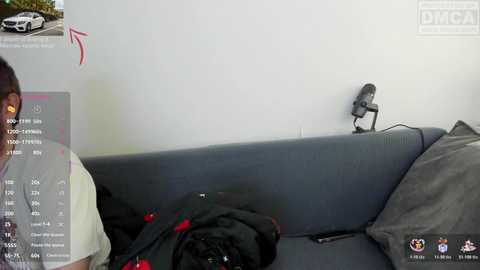 A video shows a man in a white shirt recording a video on a grey couch with a black jacket and camera.