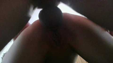 Video of a close-up view of a woman's anus, with a small, dark object partially inserted, possibly a sex toy. The background is blurry and indistinct.