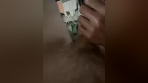 A close-up video of a person's hands holding a small, white, rectangular object, partially obscured by blurry, brownish background.