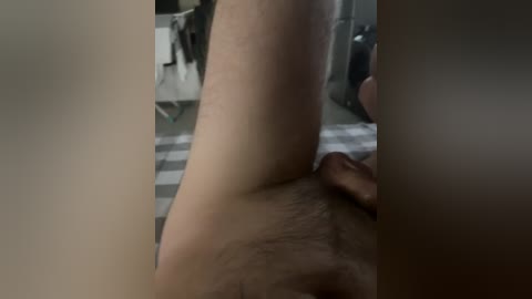 A video of a man's lower torso and genitals, positioned in a dimly lit, cluttered room with a gray and white striped rug.