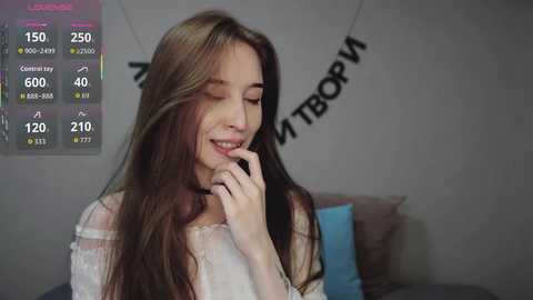 Video of a smiling young woman with long brown hair, wearing a white lace top, against a grey wall with a digital temperature display and \"VIVA\" banner.