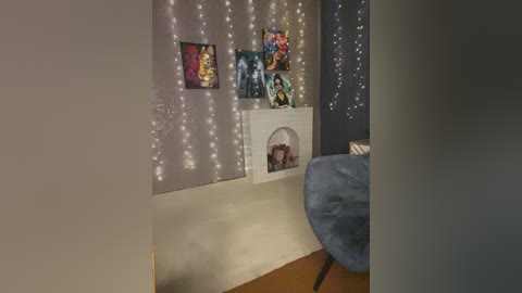 Video of a cozy room with a gray wall adorned with string lights, a small white fireplace with figurines, and a plush blue armchair.