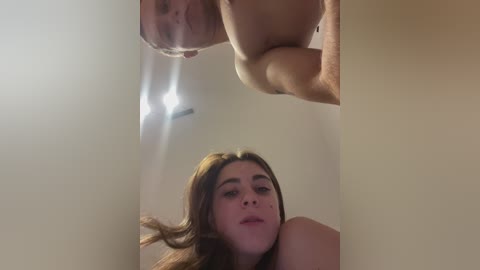 Video of a young woman with long brown hair and fair skin, seen from below, looking up at a mirror.