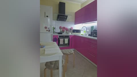 A video of a modern kitchen with vibrant magenta cabinets, white countertops, and a small table with two chairs. The space is bright, with a white tiled floor and a minimalist design.