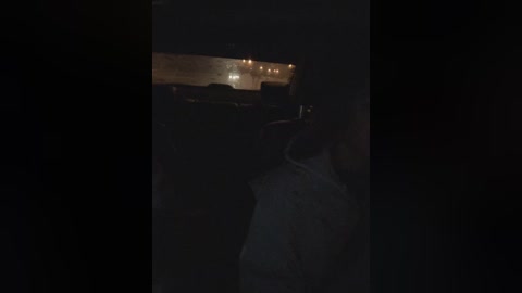 A dimly lit video of a person in a dark jacket, standing near a lit building with a glowing, textured wall, hinting at a military or industrial setting, likely at night.