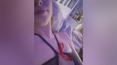 Video of a young, fair-skinned woman with blonde hair, wearing a black bra, lying on a bed with a red lipstick tattoo on her chest.