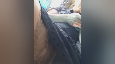 A video showing a close-up of a person's arm with a tattoo, wearing a black shirt, and a teal shirt, partially obscured by another person's hand. The background is out of focus.