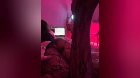 Video of a woman in a lace bra and panties, lying on a bed with a computer monitor displaying text in a dimly lit, red-lit room.