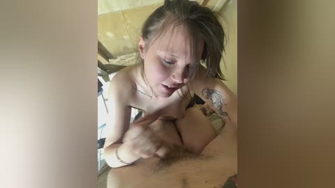 A video captures a young, nude woman with fair skin, long brown hair, and a tattoo on her left arm, performing oral sex on a man with a hairy pubic region.