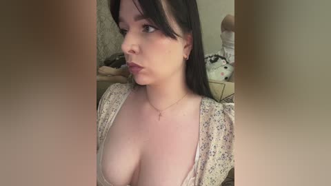 Video of a fair-skinned woman with dark hair and a low-cut floral dress, seated in a bedroom with stuffed animals.