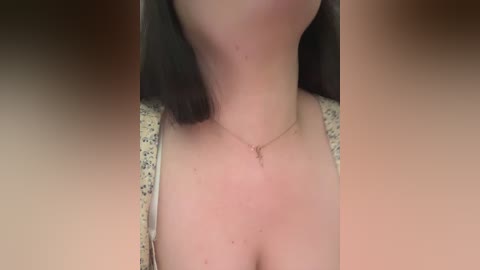 Video of a fair-skinned woman with straight, shoulder-length brown hair, wearing a floral-patterned top and a delicate necklace, with the background blurred.