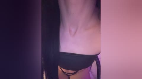 Video of a pale-skinned woman's bare midriff, wearing black lingerie with a strappy design, partially obscured by a dark garment. The background is a gradient of dark to light purple hues.