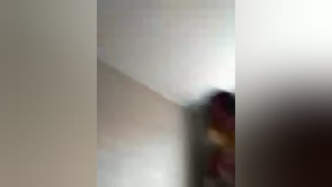 A blurred video shows a person with a dark complexion and shoulder-length hair, partially obscured by the background's soft focus. The setting is a dimly lit, narrow hallway with beige walls.