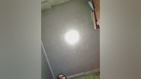 A video of a ceiling with a textured, greyish-brown finish and a bright, circular light fixture. The ceiling angles downwards, partially revealing a person's head and shoulders in the bottom left corner.