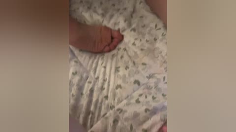 A close-up video of a hand gently smoothing out a white bedsheet with small green and grey patterned birds, taken in a dimly lit room.