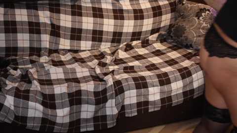 A video of a woman wearing black lace lingerie, reclining on a brown and white checkered couch with a ruffled skirt.