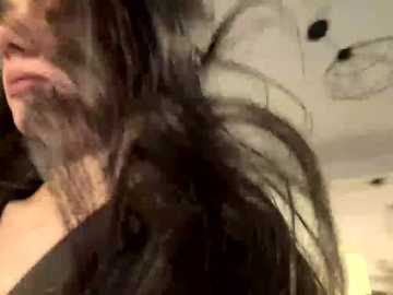 A close-up video of a woman with long, dark hair, partially obscured by a large, black, see-through hat. Her face is partially visible, showing a light complexion and closed eyes. The background is indistinct, likely indoors with a ceiling light.