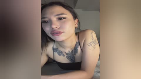 Video of an Asian woman with long black hair, light skin, and black lace top, featuring detailed floral tattoos on her chest.