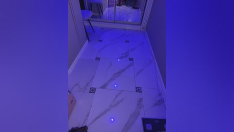 Video of a sleek, modern bathroom floor with white marble tiles, glowing blue LED lights, and a reflective mirror. The space is dimly lit, giving a cool, futuristic ambiance.