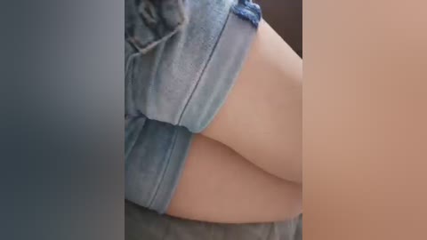 A close-up video of a woman's pale, smooth skin, partially covered by light blue denim shorts, featuring a blurred background.