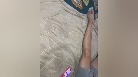 Video of a person lying on a beige quilted blanket, wearing gray shorts, with a red smartphone displaying a white screen, and a colorful patterned pillow in the background.