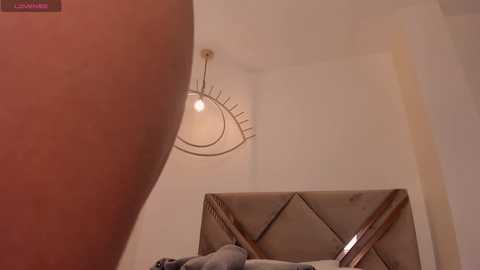 Video of a beige, tufted headboard with a plush grey throw pillow, featuring a large, round, modern chandelier with a geometric design.