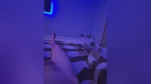 A video in a dimly lit room with a blue light filter, showing a person's legs stretched out on a bed with a striped blanket, partially visible.