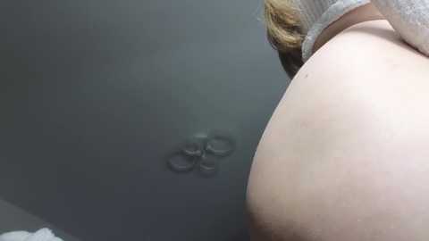 A video captures the bare, pale, round buttocks of a person from a side angle, with a grey ceiling and a small, circular, grey light fixture visible in the background.
