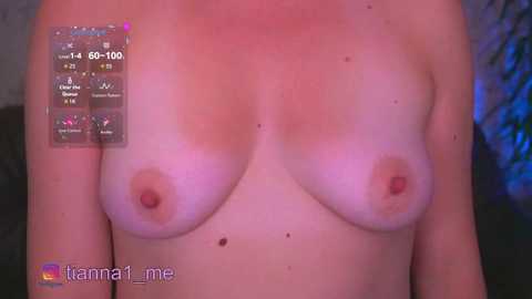 A video of a topless, fair-skinned woman with small, perky breasts, slightly tanned, standing against a blurred, dark background. A digital overlay displays temperature and health metrics in the upper left corner.