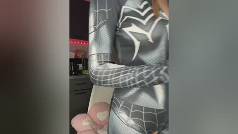 Video of a person in a Spider-Man costume, holding a toy Spider-Man figure, with a modern kitchen in the background.