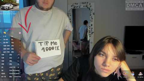 A video shows a man holding a sign saying \"Tip Me 1000k\" and a woman with long hair, both in a modern living room.