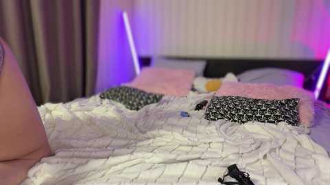 Video of a person in bed with a white quilted comforter, featuring a black and white patterned pillow, and a purple-lit bedroom background.