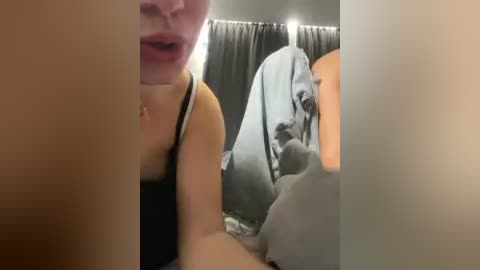 A video shows a partially obscured woman in a black tank top, leaning over a man in a gray shirt. The background features a dark curtain and a blurred orange light source.