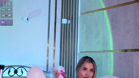 Video of a young woman with blonde hair, holding a pink drink, in a modern room with white walls and vertical blinds.